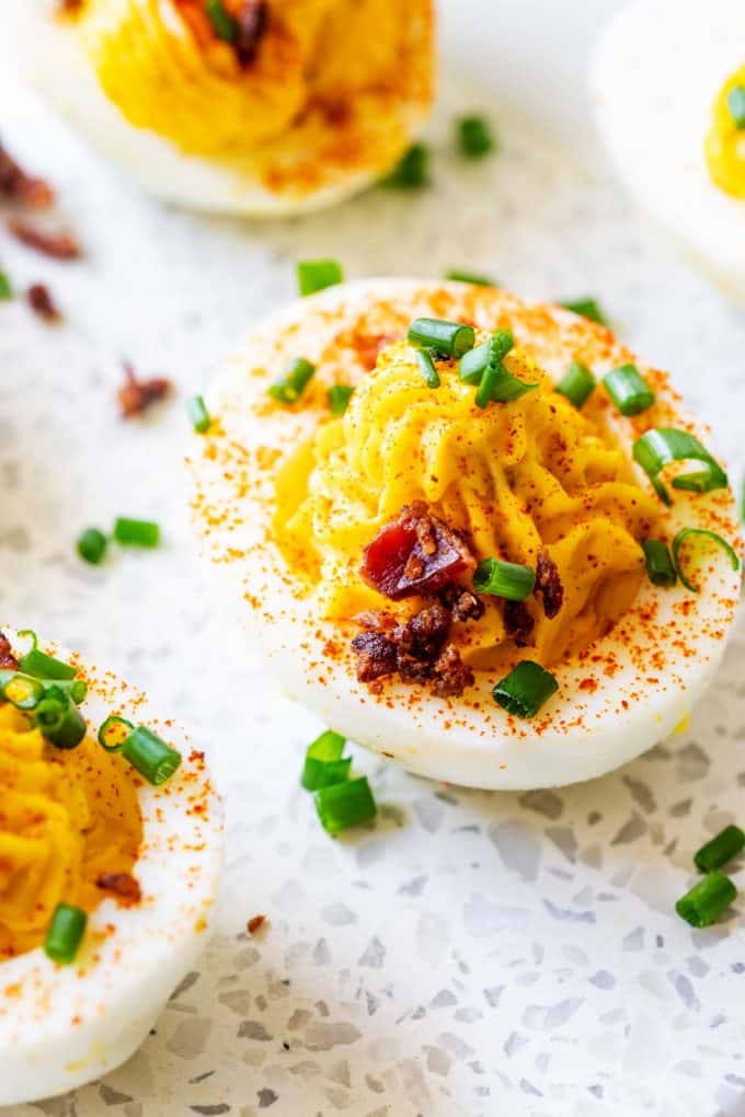 Photo of a white platter with keto deviled eggs garnished with bacon, paprika, and parsley.