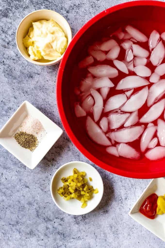 Photo of a red bowl filled with ice surrounded by the ingredients for deviled eggs.
