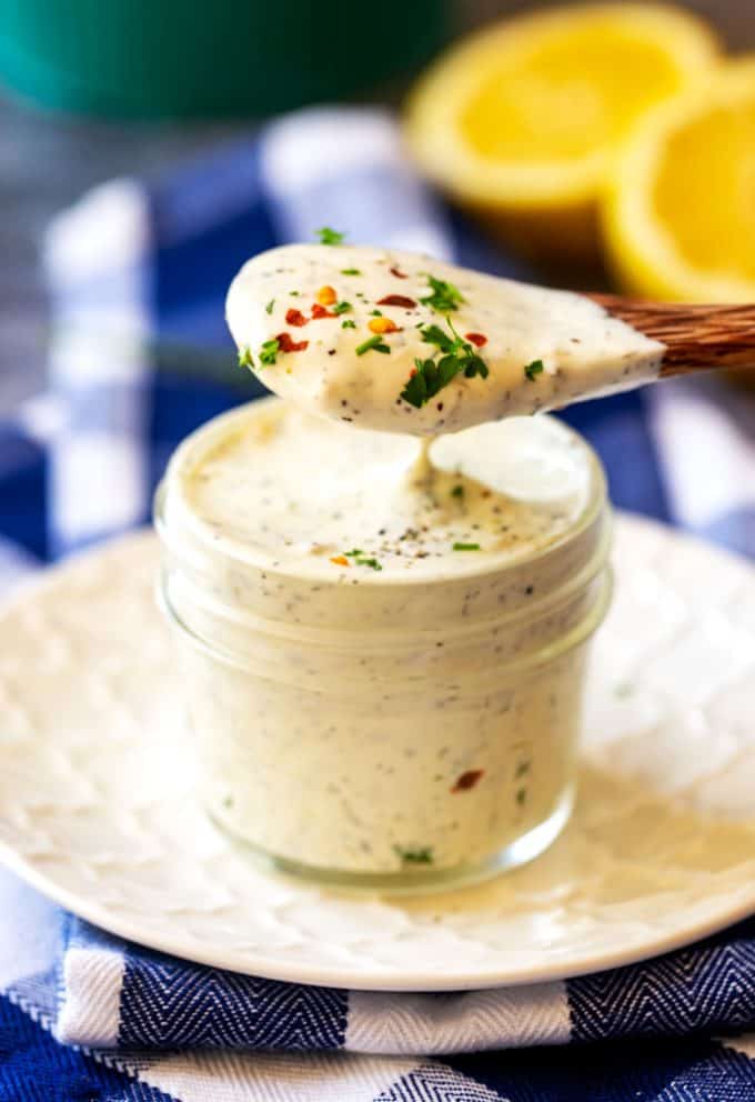 Photo of a spoon of creamy Keto Ranch Dressing being lifted from a small jar.
