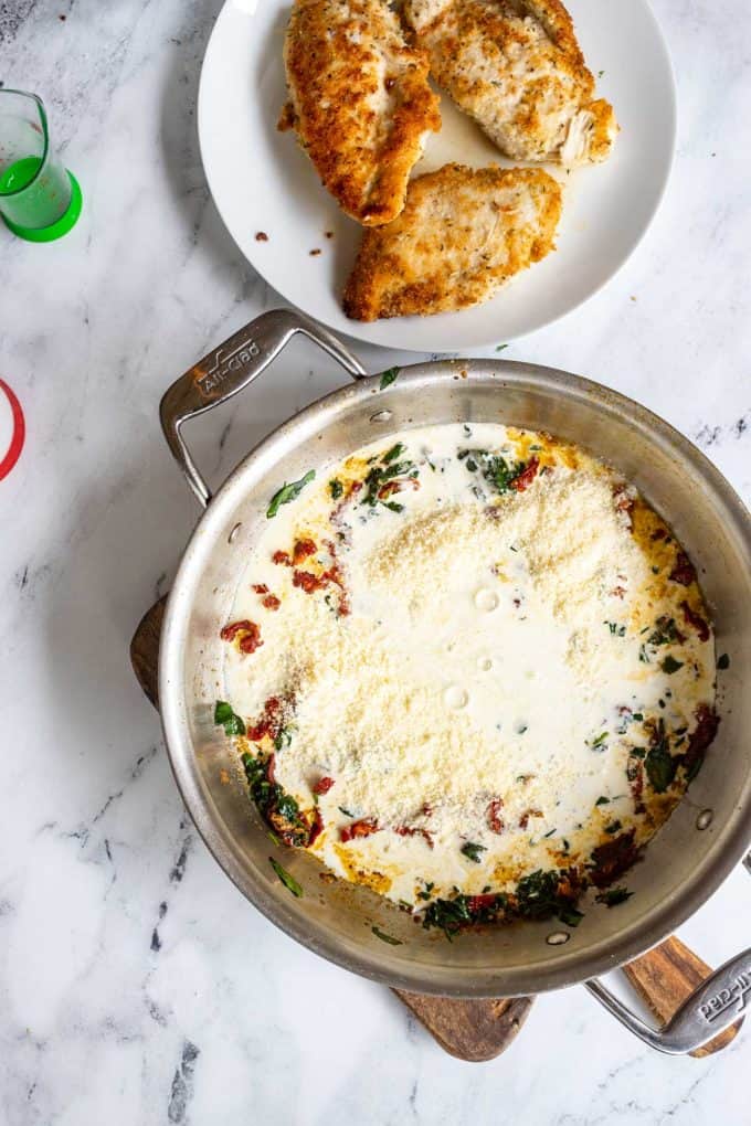 Photo of a skillet with the ingredients for a cream sauce has been added to spinach and sundried tomato.