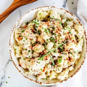 Square overhead photo of a rustic bowl with Keto Potato Salad with Cauliflower and a spoon next to it.