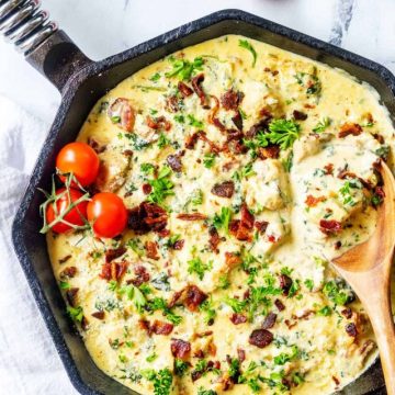 Photo of a skillet with chicken carbonara with a spoon in it garnished with on the vine tomatoes.