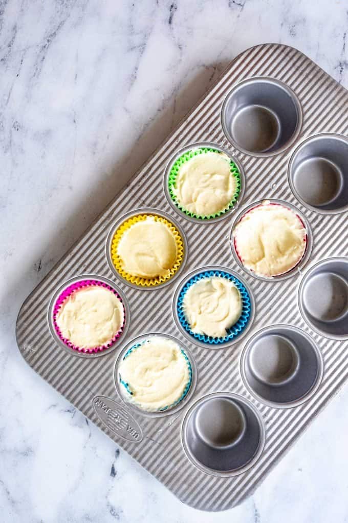 Photo of a muffin tin lined with silicone liners and filled with cheesecake batter.