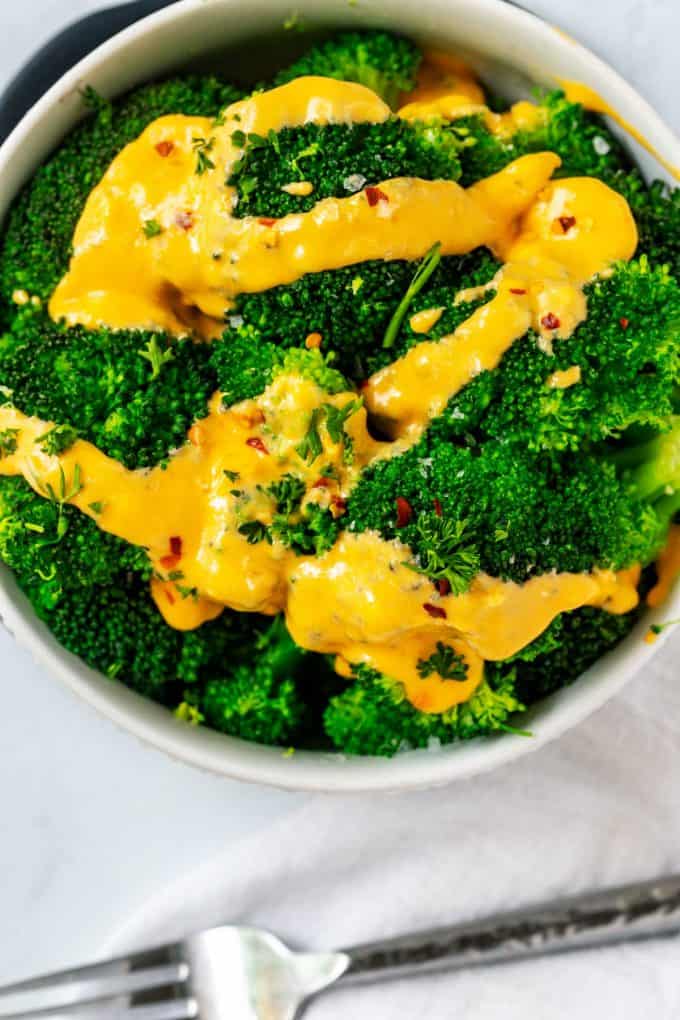 Overhead photo of a bowl of steamed broccoli with keto cheese sauce drizzled on top.