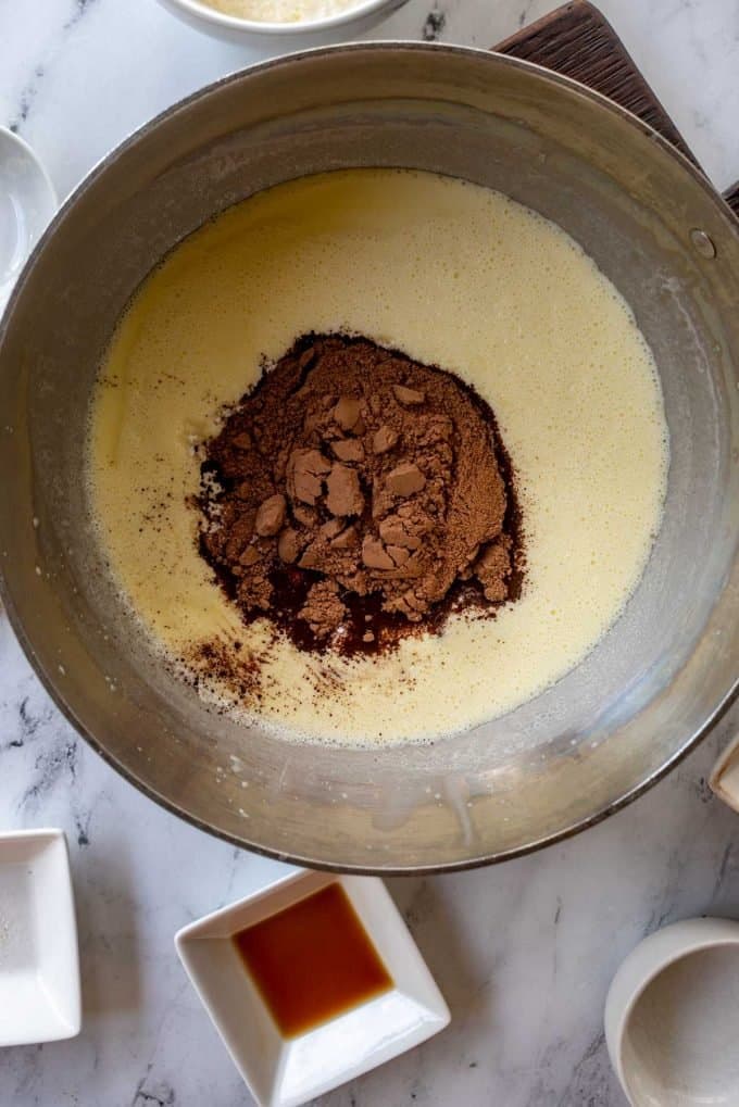 Overhead photo of a sauce pan with heavy cream that has had sweetener and cocoa powder added to it.