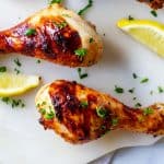 Close up square photo of chicken legs on a white board garnished with parsley.