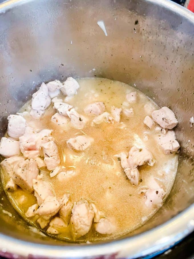 Photo of seasoned chicken cubes, onion, garlic, and broth in an instant pot.