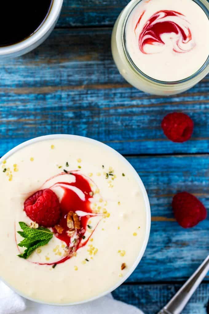 Overhead photo of keto yogurt garnished with a raspberry, raspberry sauce, mint, pecans, and hemp seeds.