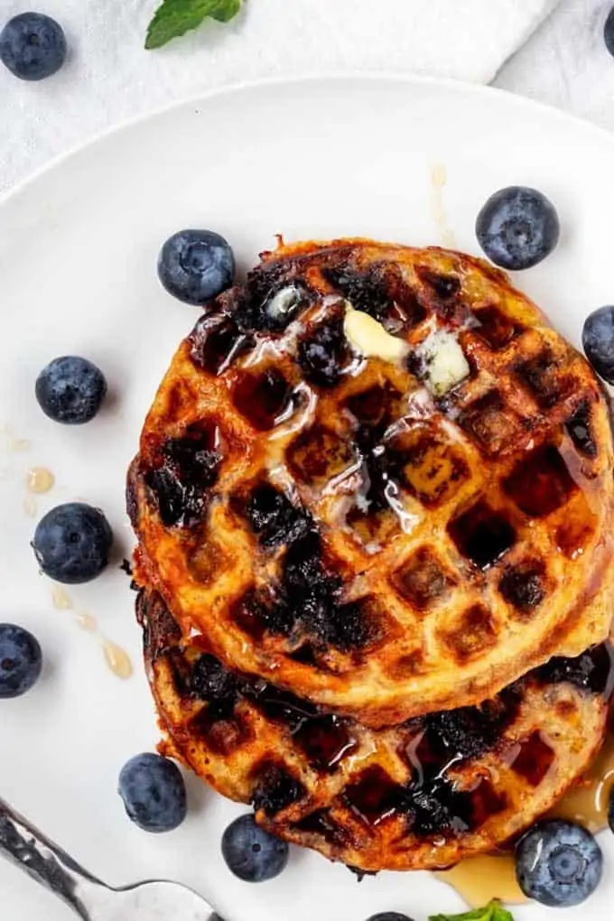 Photo of two blueberry chaffles on a white plated topped with sugar-free syrup and blueberries.