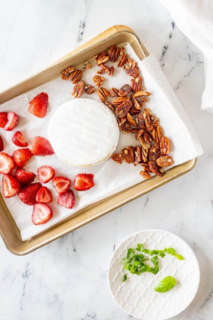 Photo of a baking sheet with strawberries and brie that have been partially roasted with pecans next to it.