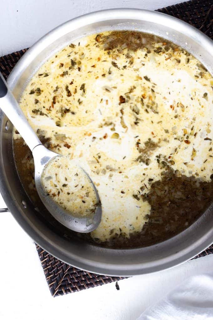 Photo of a skillet where cream has been added to broth and onions with seasonings.
