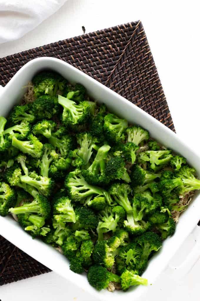 Photo of a white casserole dish with shredded chicken and broccoli on top of it.