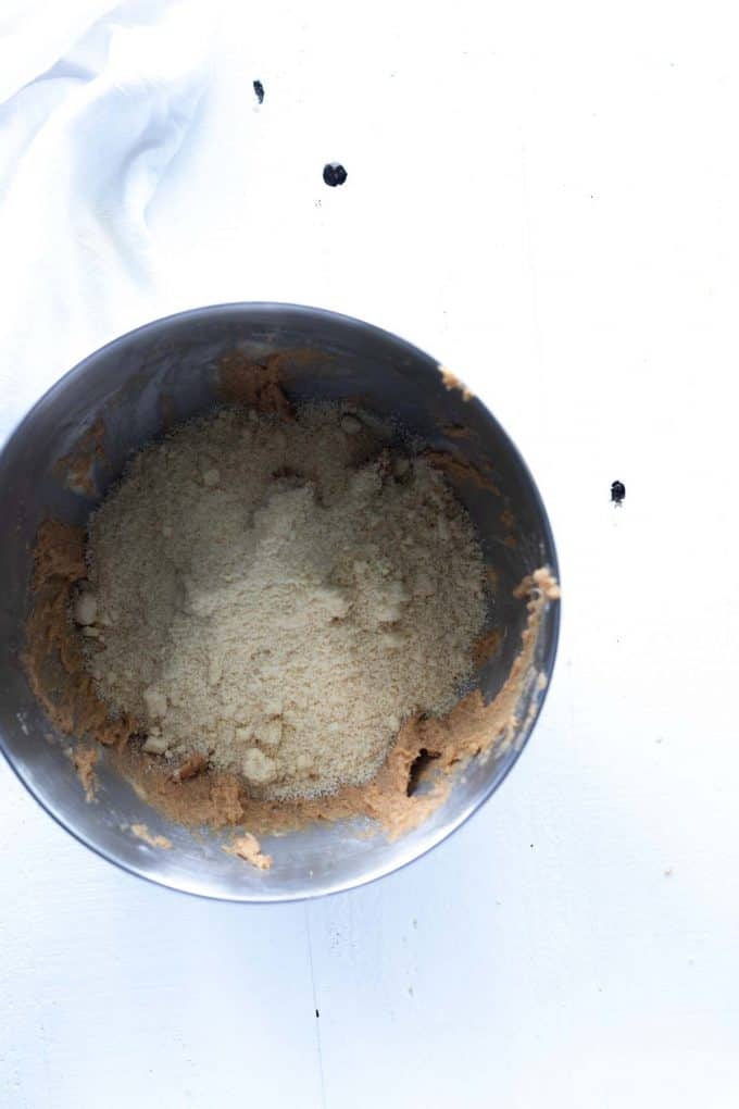 Photo of almond flour being added to cookie batter in the bowl of a stand mixer.