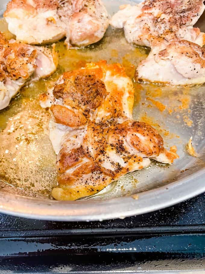 Photo of chicken thighs being cooked in a large skillet.