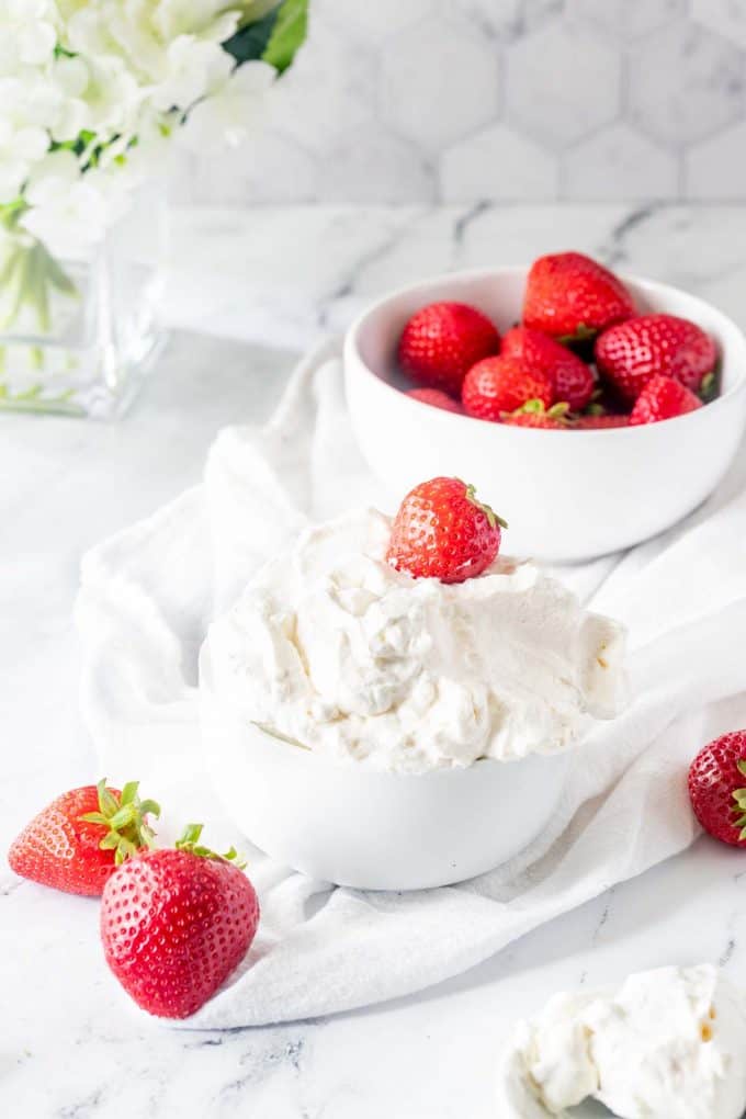 Side photo of a bowl of keto whipped cream surrounded by strawberries.