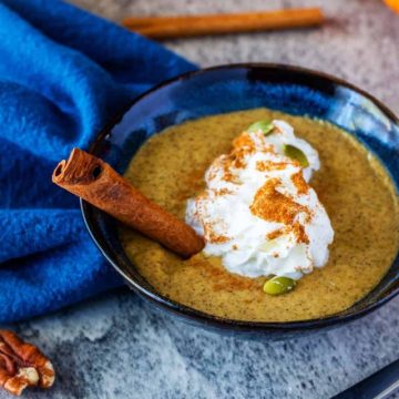 Keto pumpkin chia pudding in a small blue bowl garnished with whipped cream, pumpkin seeds, and a cinnamon stick.
