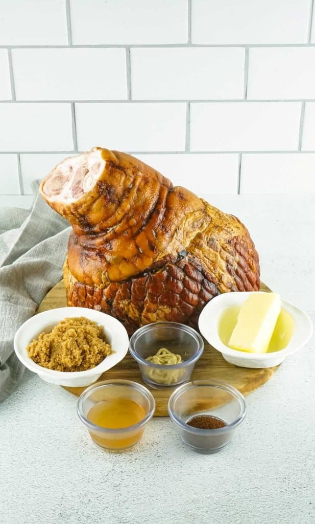 Photo of a ham with brown sugar substitute, dijon, butter, vinegar, and cloves sitting in front of it.