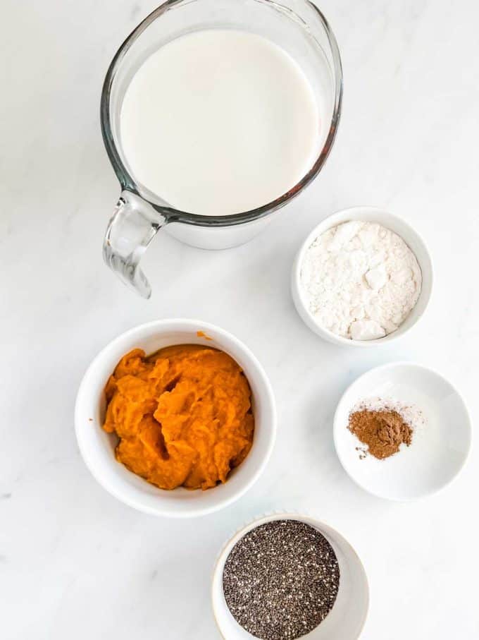 Overheat photo of heavy cream, almond milk, swerve, pumpkin pie seasoning, pumpkin puree, and chia seeds in prep bowls.