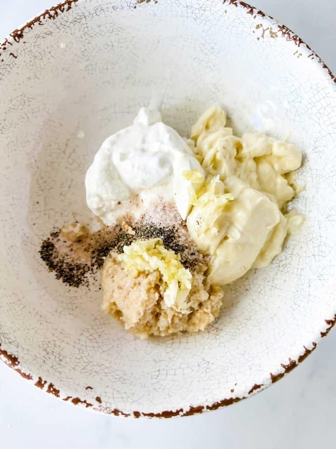 Photo of mayonnaise, sour cream, prepared horseradish, garlic, salt, and pepper in a bowl.