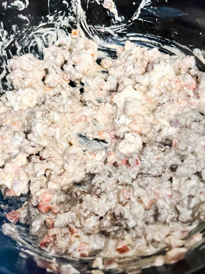 Photo of ground beef, red pepper, and red onion that has had creamed cheese stirred into it.