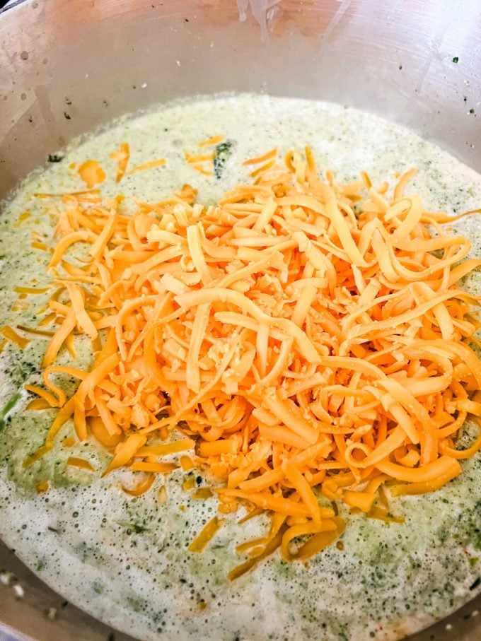Photo of a pot of broccoli soup that has just had shredded cheese added to it.