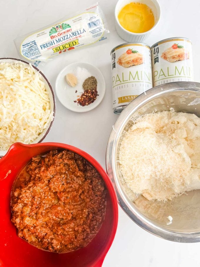 Photo of palmini noodles, garlic, seasonings, beaten egg, fresh mozzarella, shredded mozzarella, keto meat sauce, and a ricotta parmesan mixture.