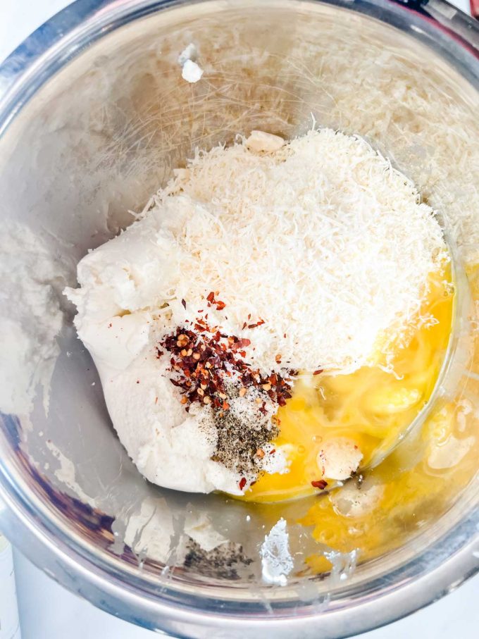 Overhead photo of ricotta, parmesan, eggs, and seasonings in a metal bowl.