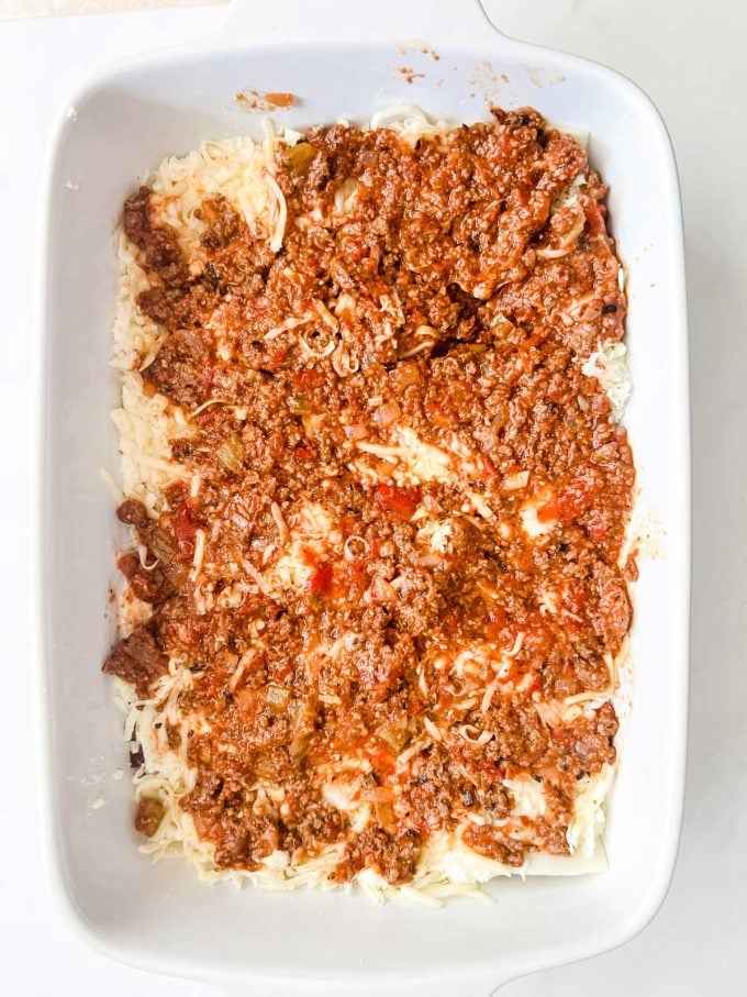 Meat sauce on top of shredded cheese and ricotta cheese in a casserole dish.