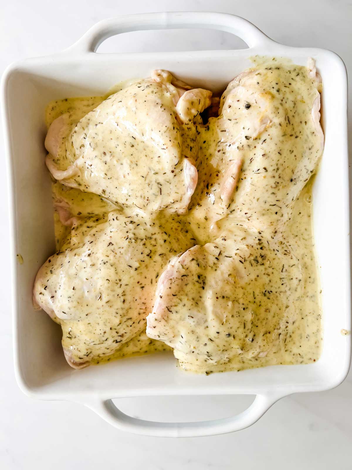 Overhead photo of a shallow casserole dish with chicken thighs covered in marinade.