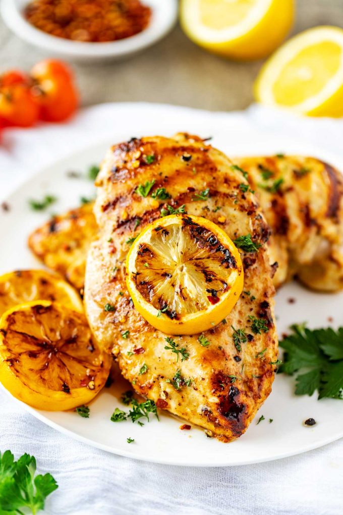 Photo of a white plate of grilled lemon pepper chicken garnished with a lemon and parsley.