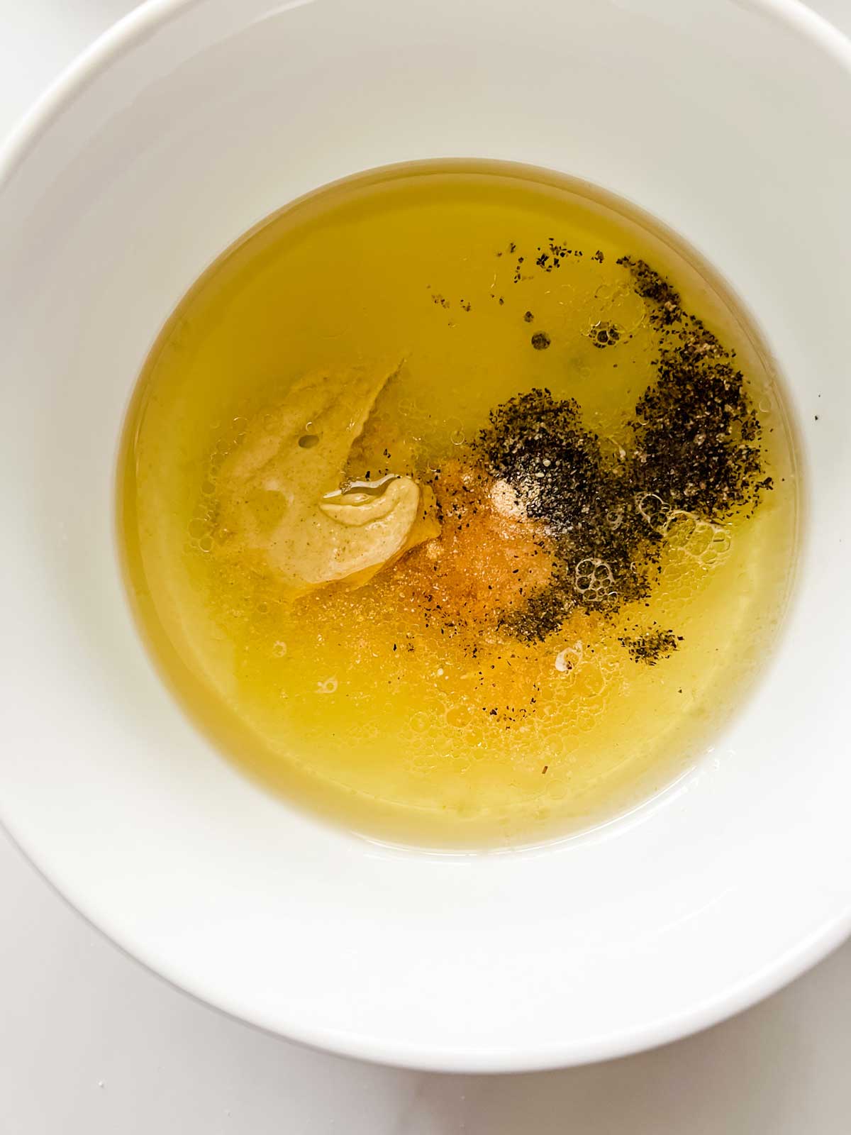 Close up photo of a small bowl of oil, lemon juice, mustard, and seasonings.