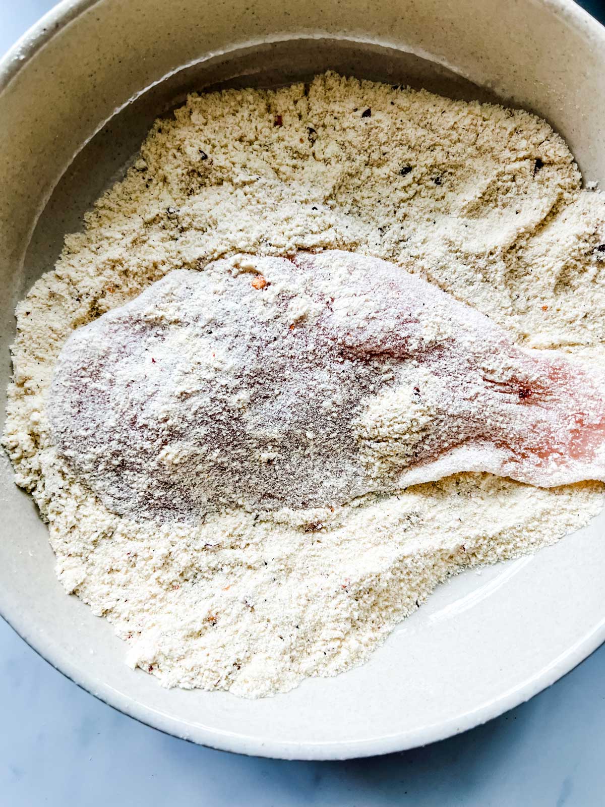 Chicken breast in a bowl of seasoned coconut flour.