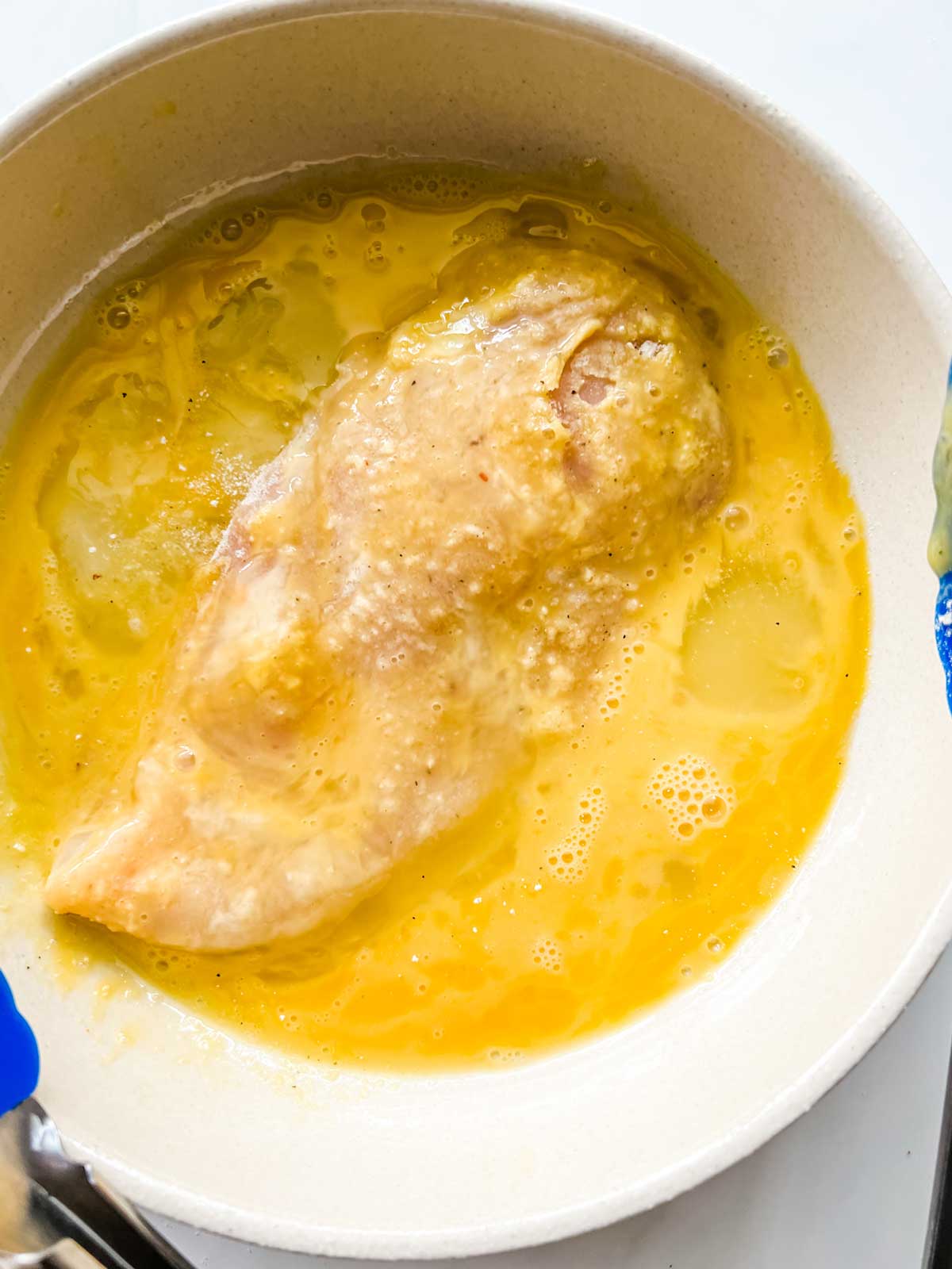 Chicken that has been dipped in coconut in a bowl of beaten egg.