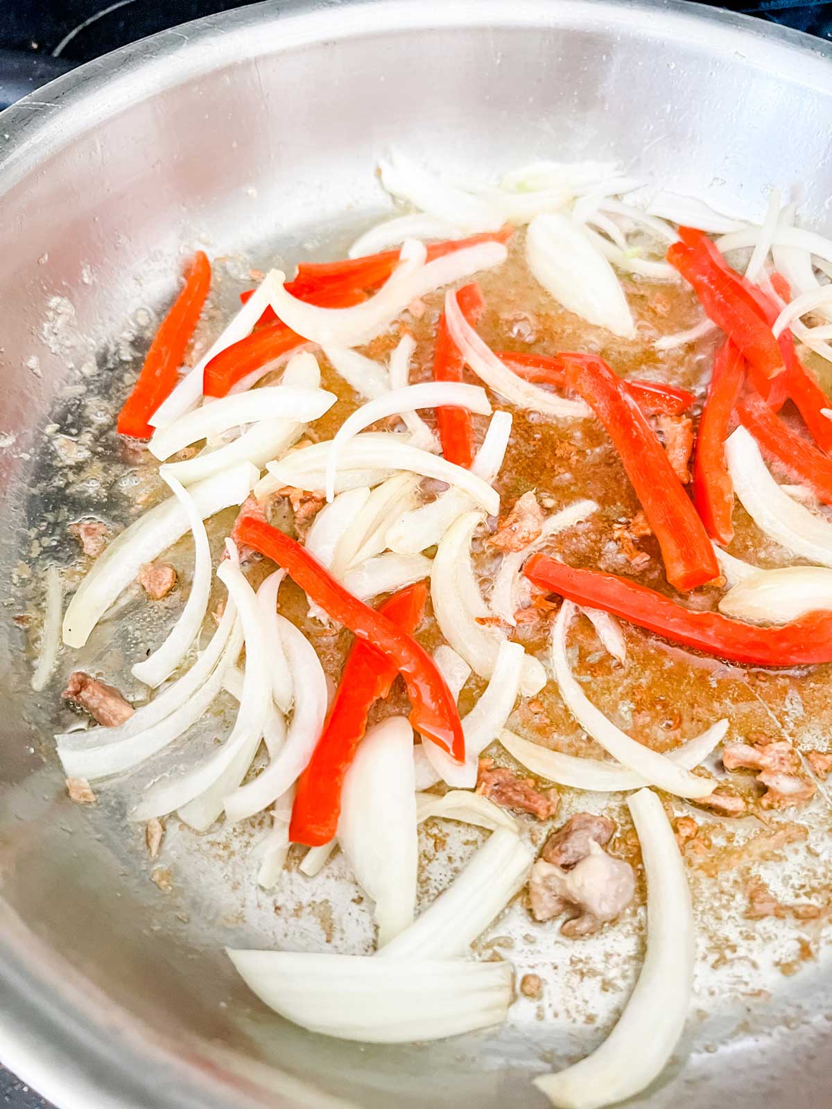 Onion and red pepper strips cooking in a skillet.
