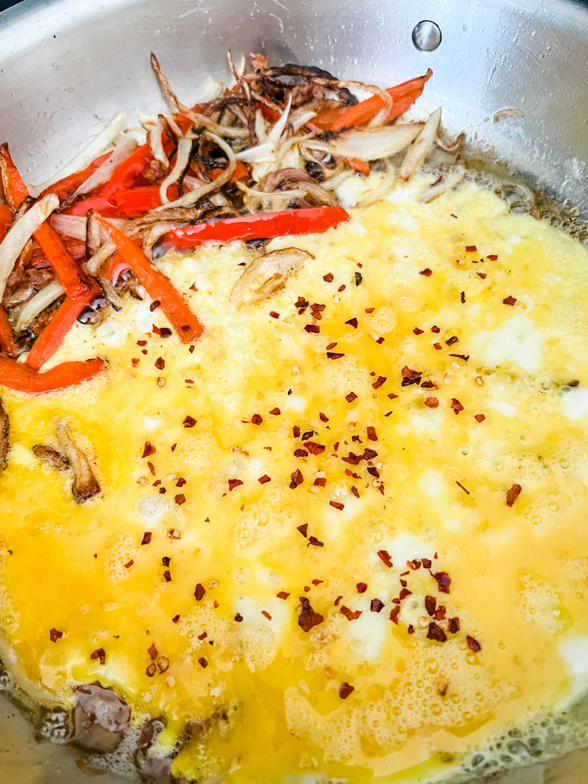 Eggs sprinkled with red pepper flakes sitting next to sauteed onions and peppers in a skillet.