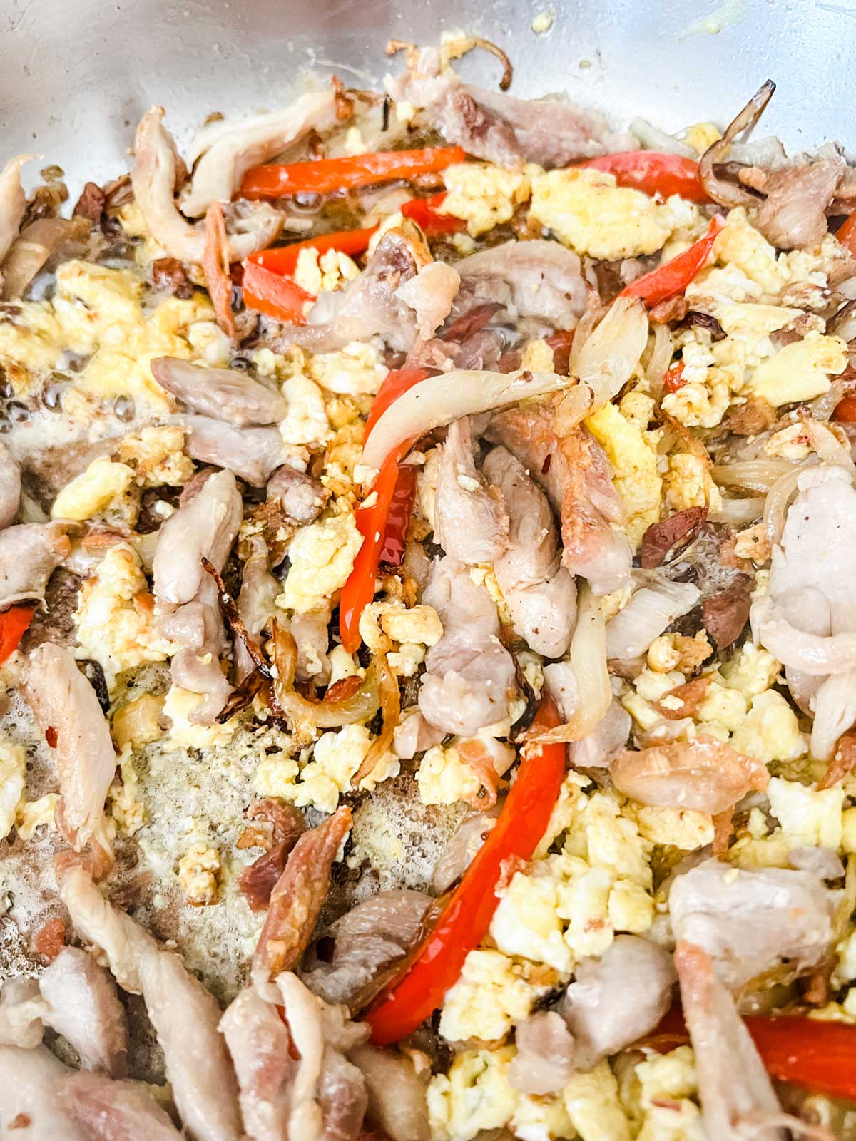 Close up photo of chicken strips, onion, red pepper, and egg in a skillet.