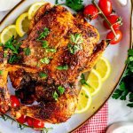 Square overhead photo of a platter with an Air Fryer Whole Chicken on it garnished with parsley and surrounded by lemons and grape tomatoes.