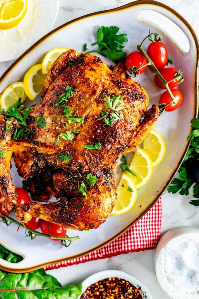 Overhead photo of a platter with an Air Fryer Whole Chicken on it garnished with parsley and surrounded by lemons and grape tomatoes.