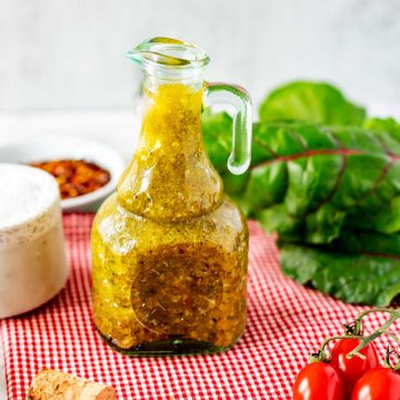Square photo of a glass dressing jar with Keto Italian Dressing sitting on a red and white napkin.