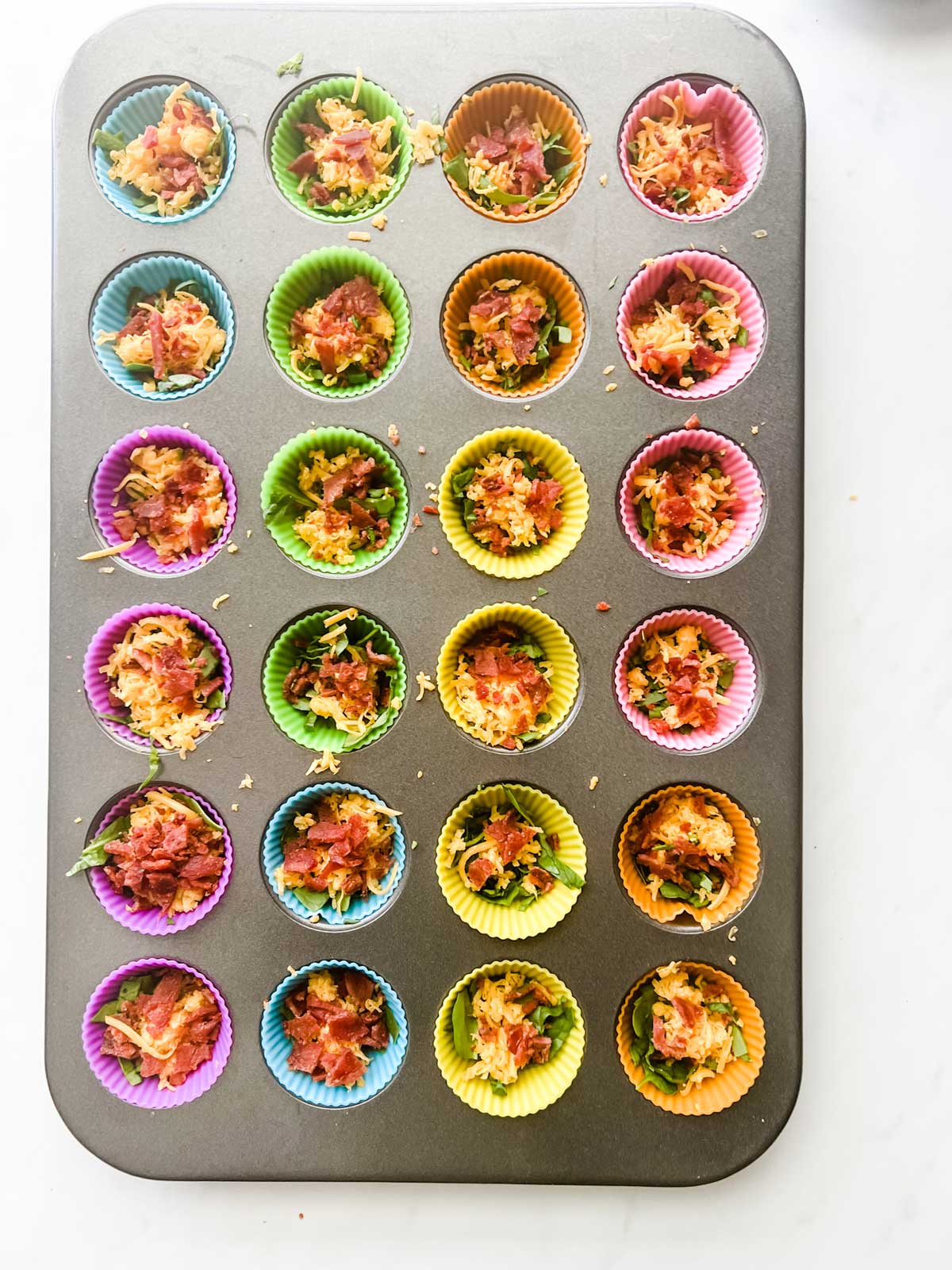 Photo of bacon, spinach and cheese in a lined mini-muffin pan.