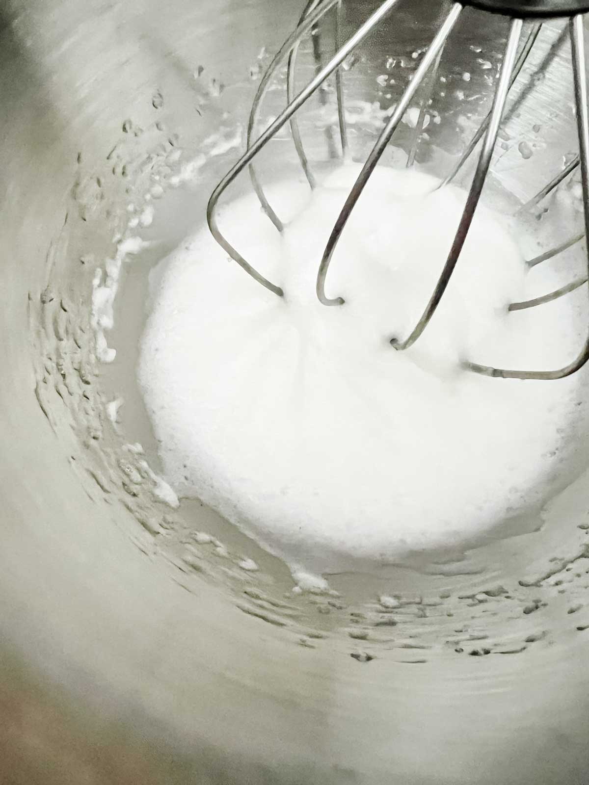Photo of egg whites being beaten in hte bowl of a stand mixer.