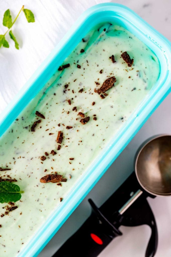 Overhead photo of a freezer-safe container of keto mint chocolate chip ice cream with an ice cream scoop on one side.