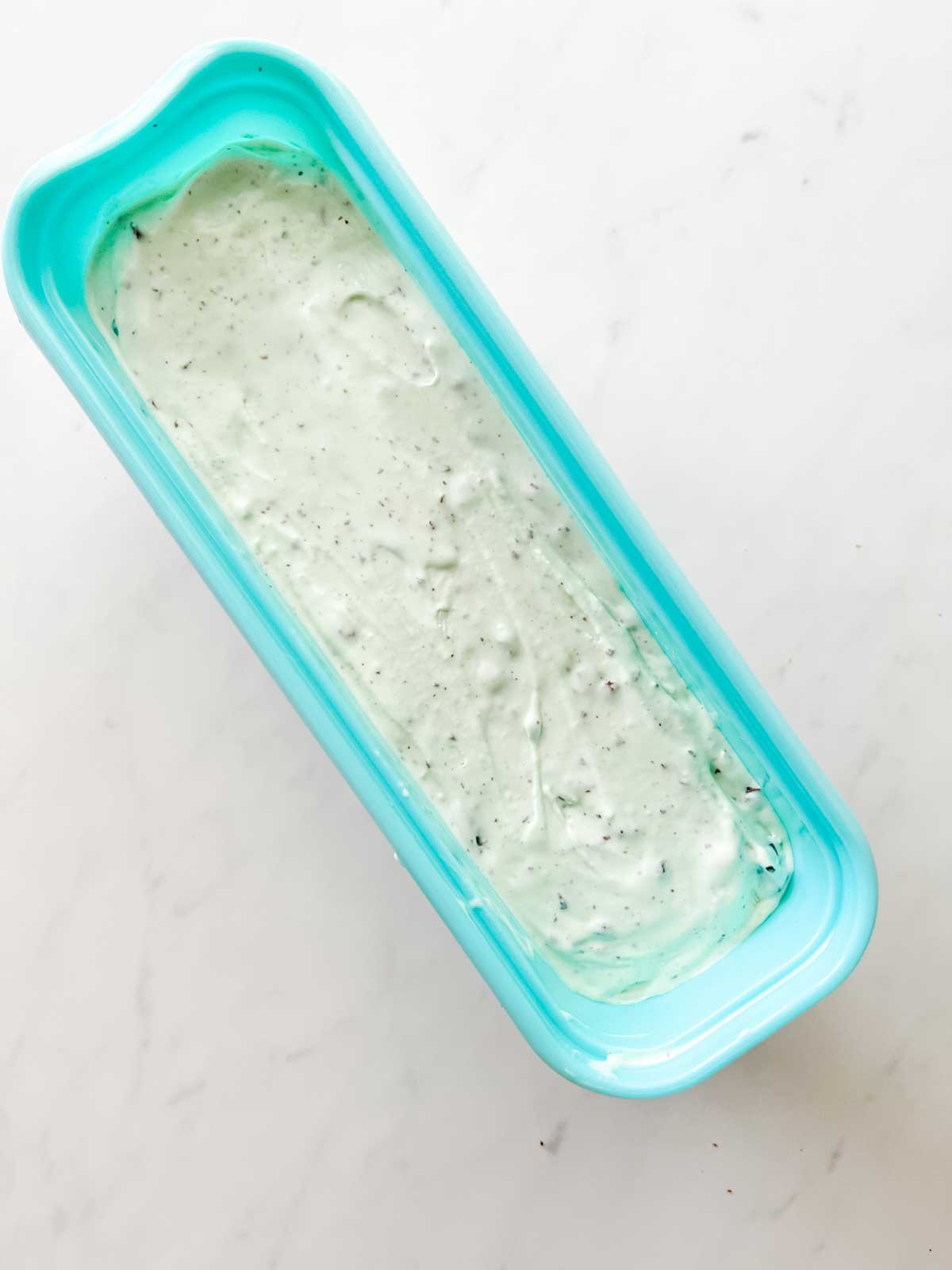 Soft keto mint chocolate chip ice cream that has been transferred to a freezer safe container.