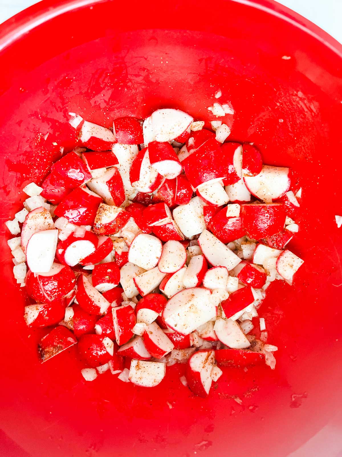 Overhead photo of a red bowl with radishes and onions that have been tossed with seasonings.