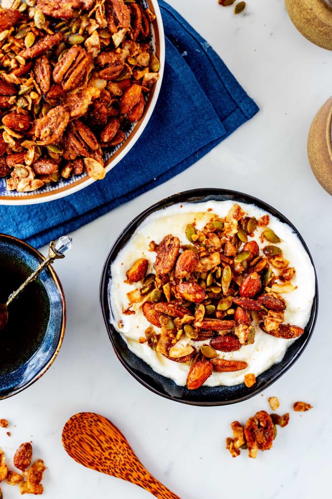 Keto granola over yogurt, with a small dish of sugar-free maple syrup and a large bowl of granola next to it.