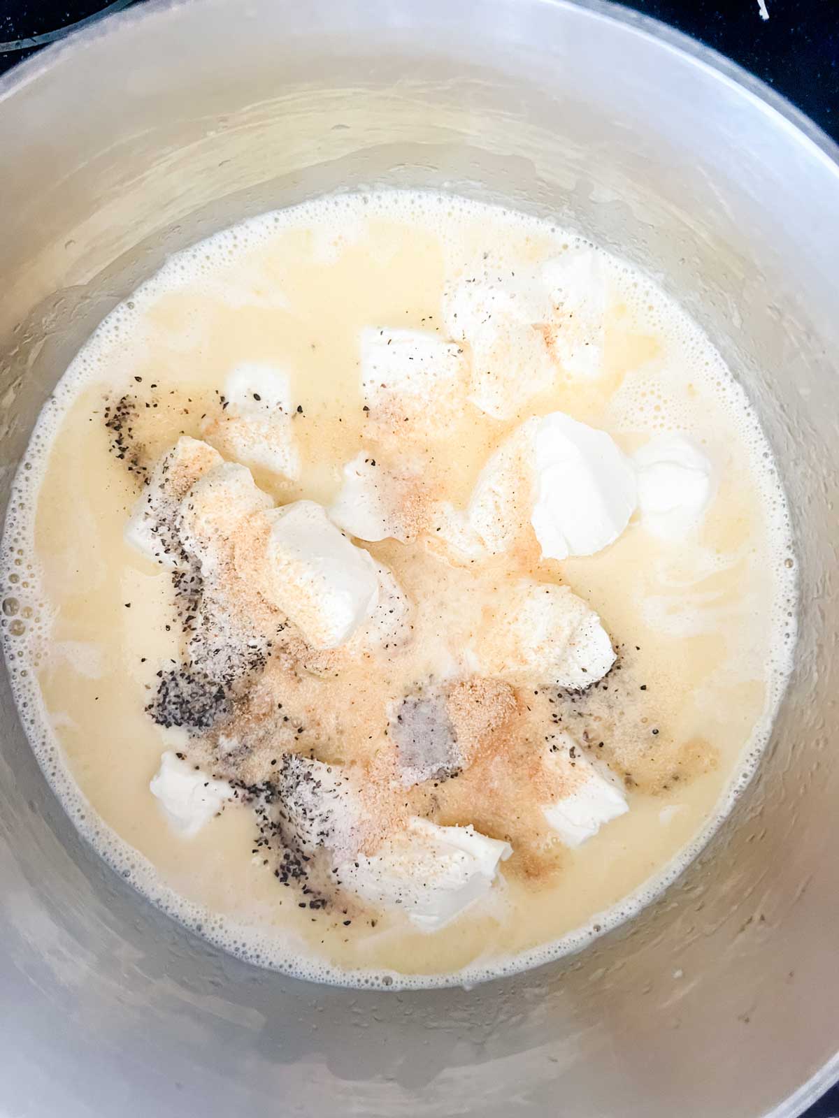 Photo of cream, butter, cream cheese, and seasonings in a saucepan.