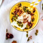 Square overhead photo of a keto pumpkin smoothie garnished with whipped cream, pecans, and pumpkin seeds.