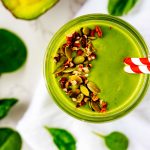Square overhead photo of a keto green smoothie garnished with pecans and pumpkin seeds.