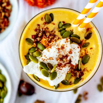 Overhead square close up photo of a keto pumpkin smoothie with a dollop of whipped cream, pumpkin seeds, and pecans.