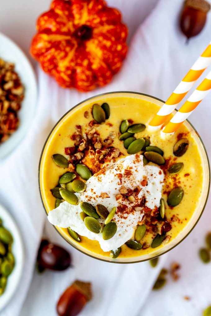 Overhead photo of a keto pumpkin smoothie garnished with whipped cream, pumpkin seeds, pumpkin pie seasoning, and pecans.